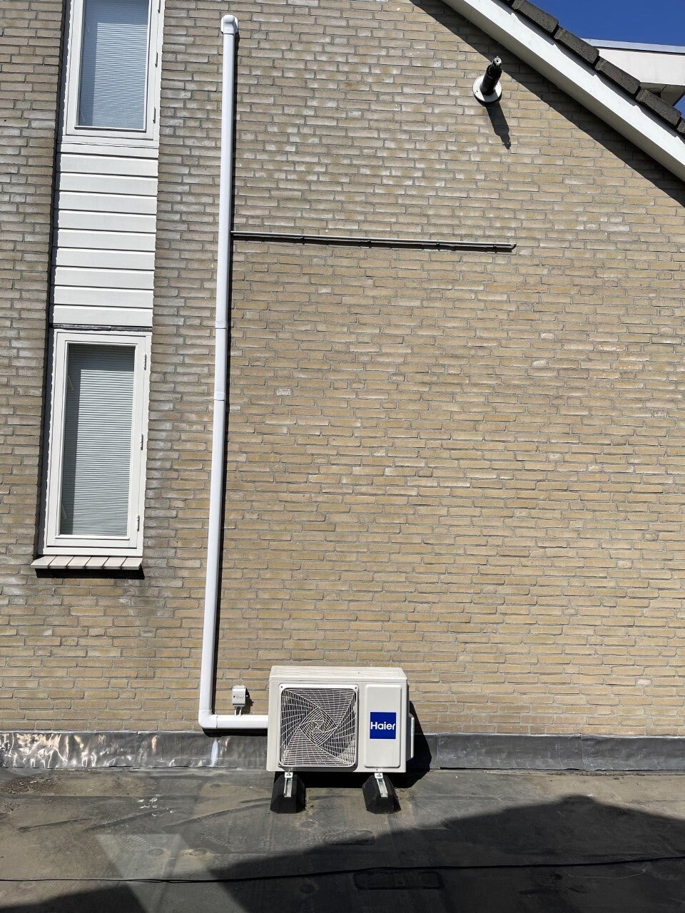 Airco-buitenunit met leidingwerk langs een gevel